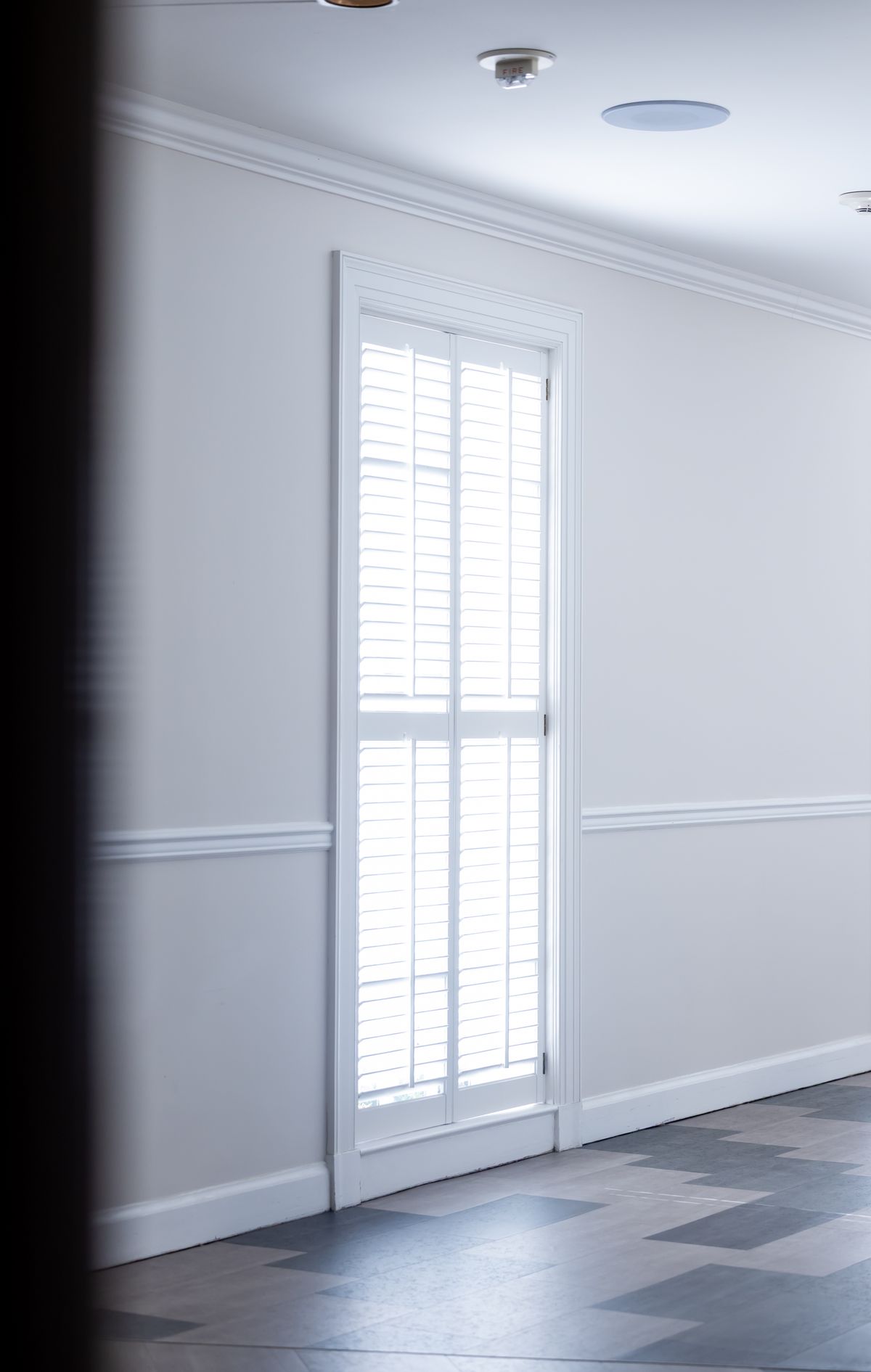A tall single California shutter set into a quiet hallway