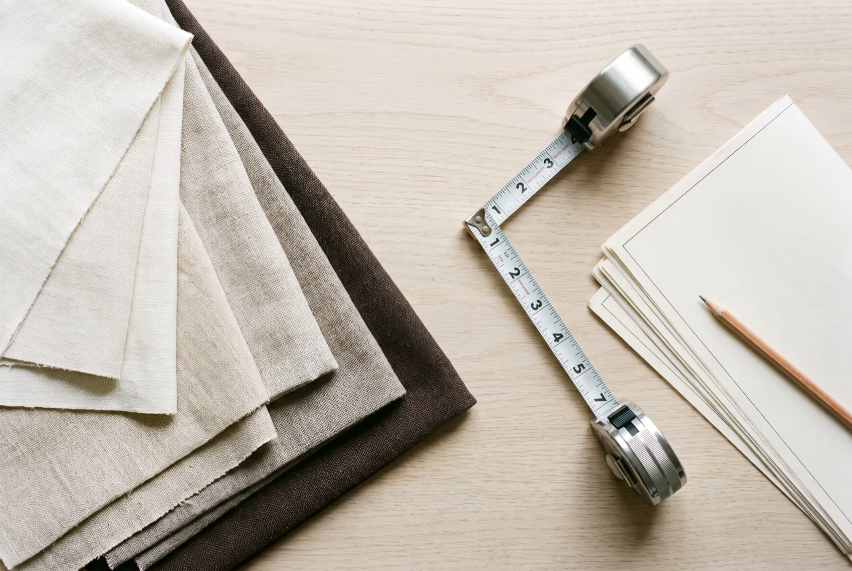 Window-covering fabric samples, a measuring tape and drawings laid out on an oak table