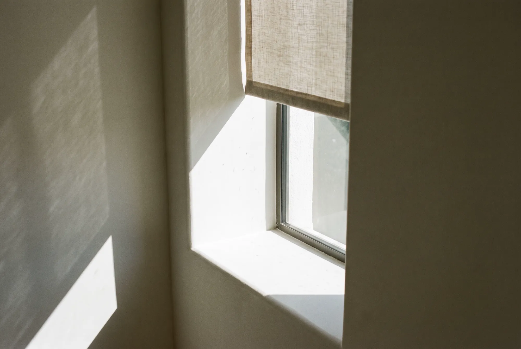 Morning light falling through a linen shade onto a plaster wall
